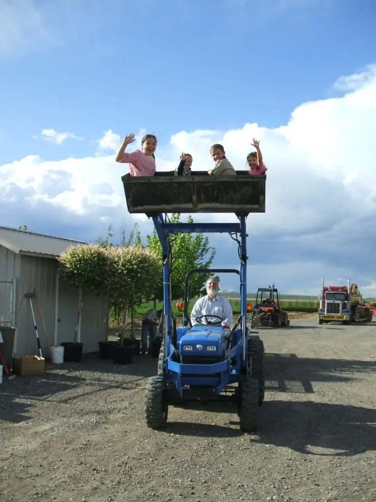Everett driving a blue tractor with four children waving from the raised loader bucket