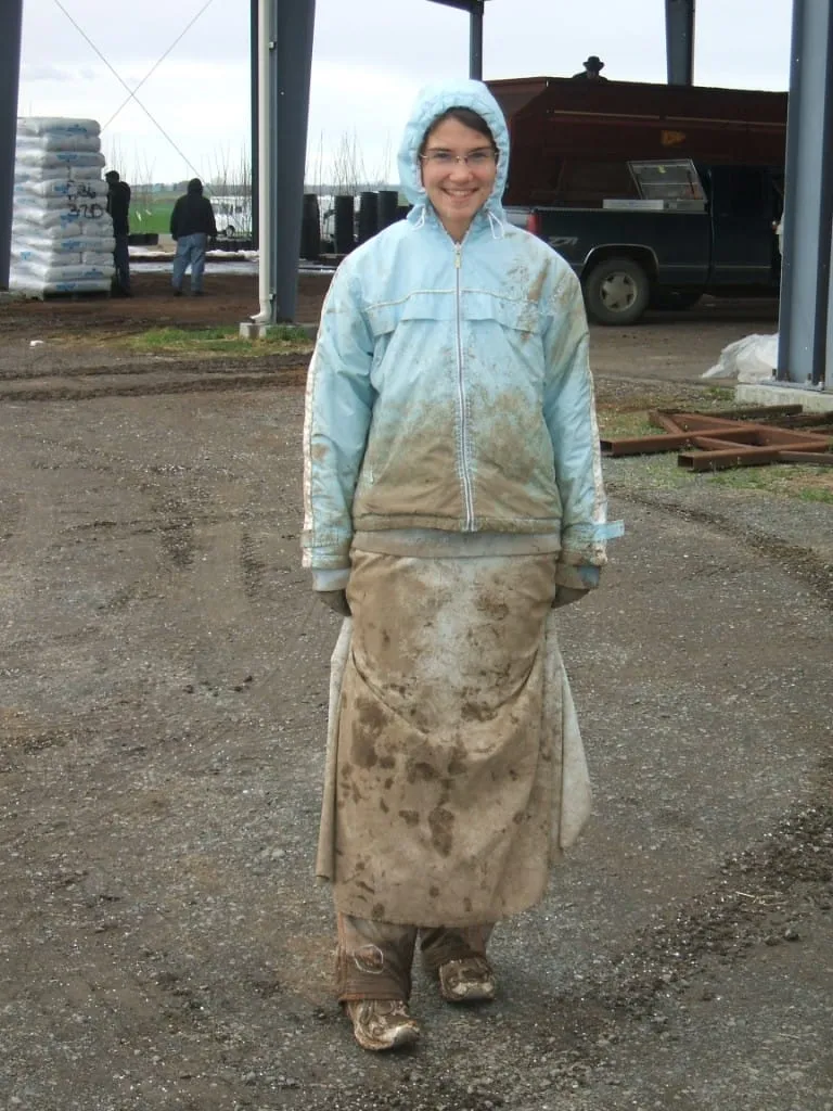 Young woman in muddy work clothes standing under a nursery barn