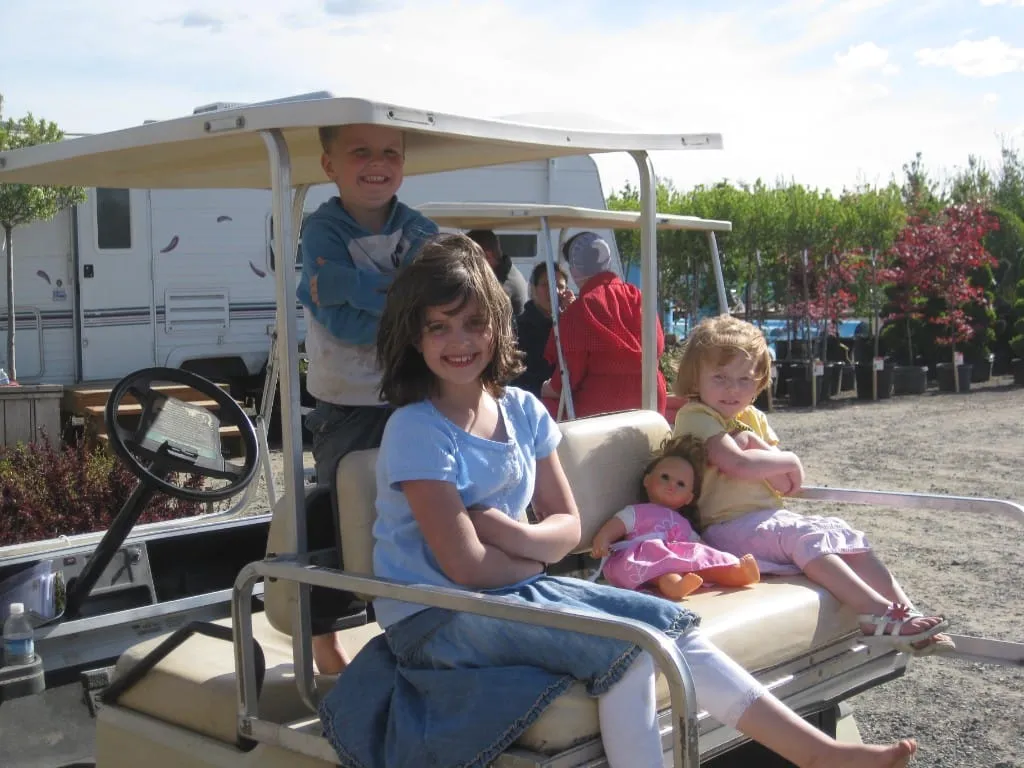 Three children smiling on a golf cart at the nursery