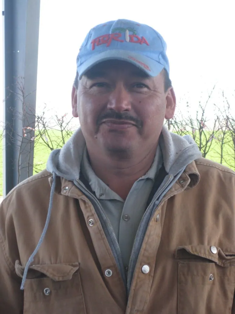 Nursery worker in a Florida cap and canvas jacket among dormant trees